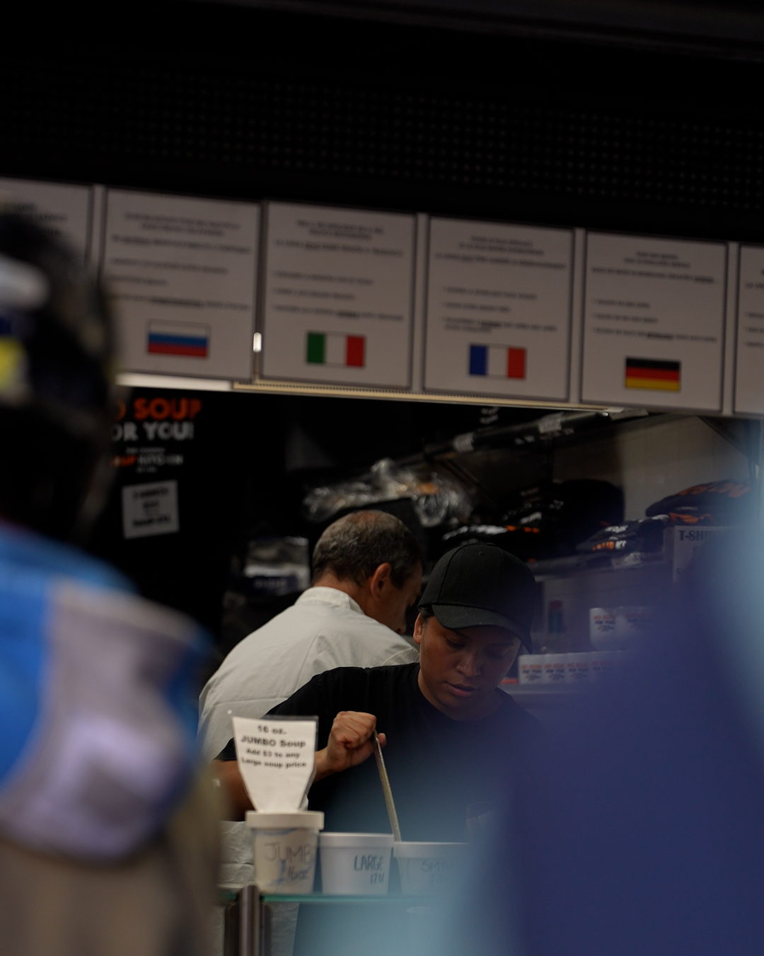 Two cooks working behind the service window at The Original Soup Kitchen, below ordering instructions posted in several languages