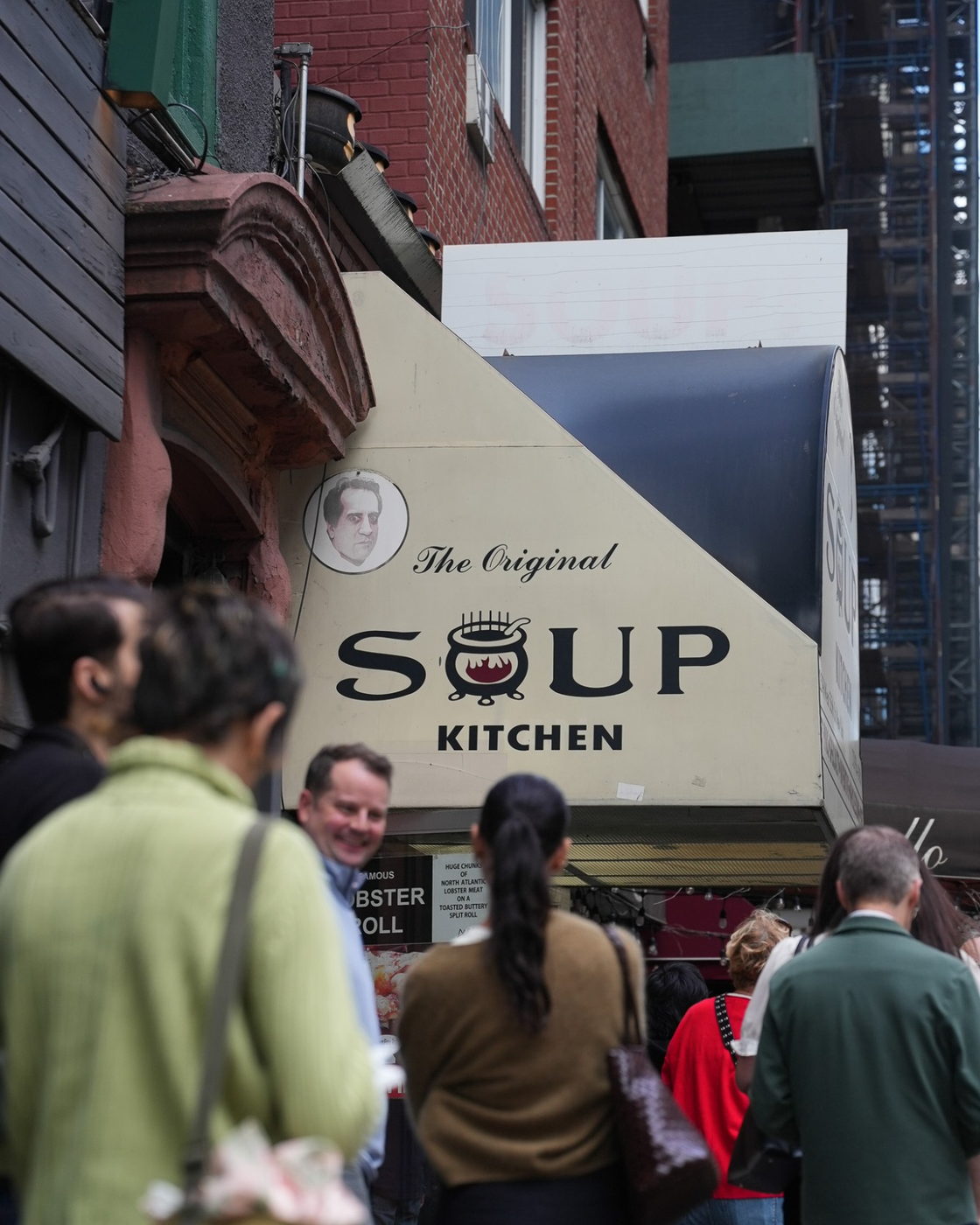 The Original Soup Kitchen awning seen from the sidewalk, with people waiting at the window
